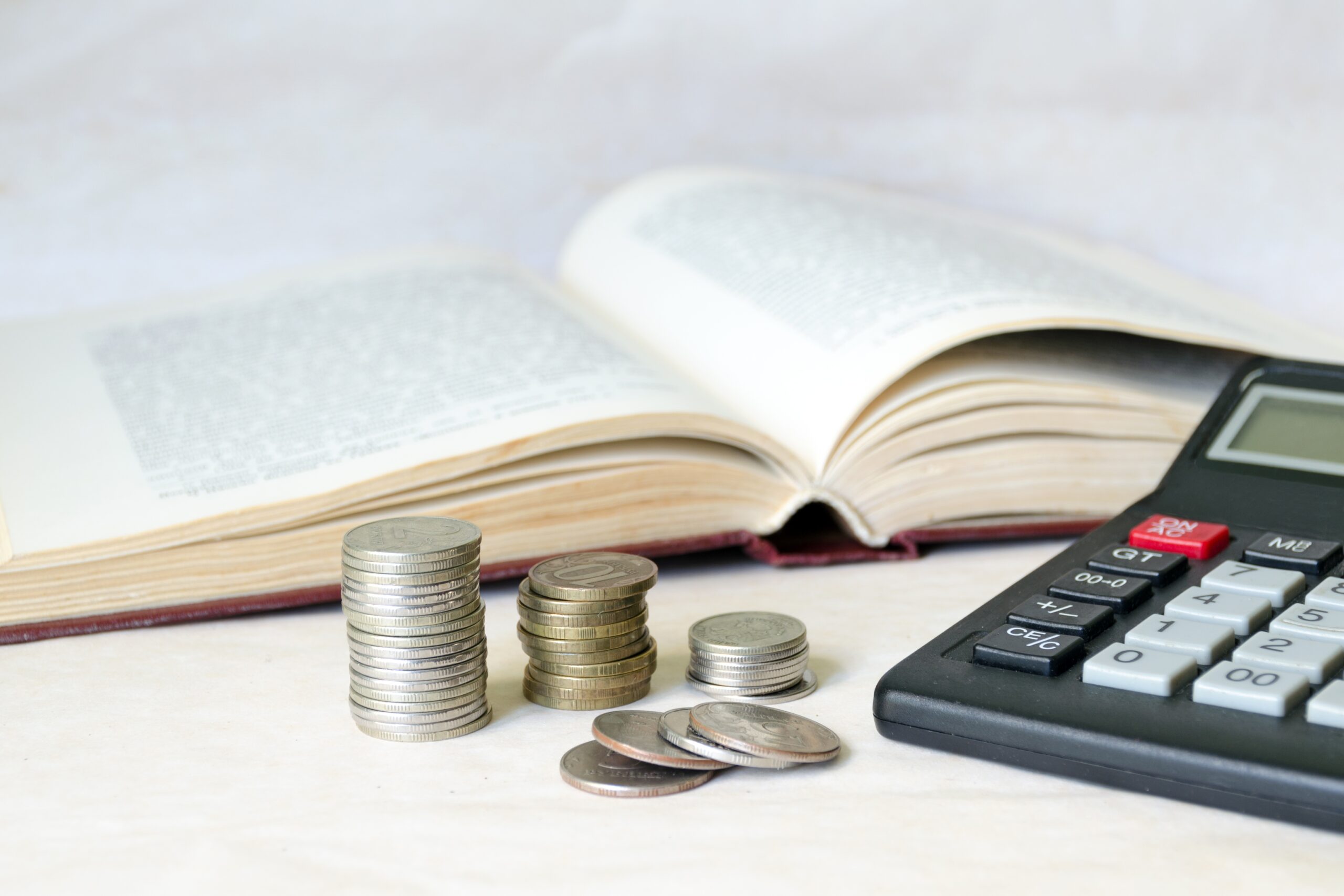 A stack of coins and a calculator in front of an open book. The